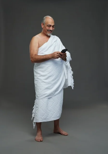 رجل عربي بملابس الإحرام يستخدم الهاتف الذكي في استوديو