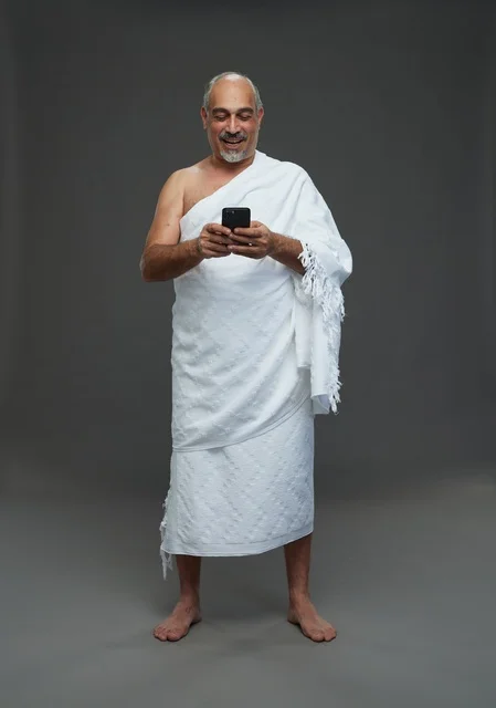Arab Man in Ihram Using Smartphone on Gray Background