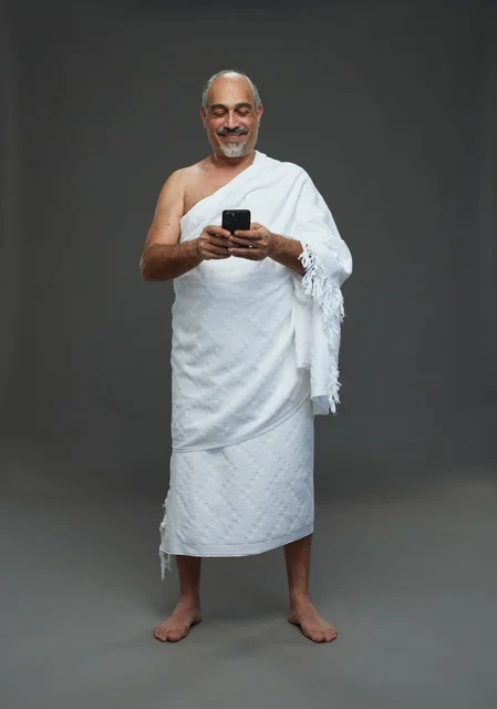 رجل عربي بملابس الإحرام يستخدم الهاتف الذكي في الاستوديو