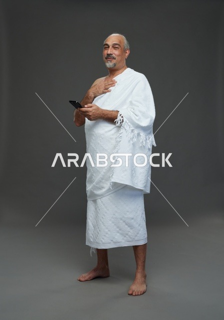 رجل عربي بملابس الإحرام يحمل هاتف ذكي في الاستوديو