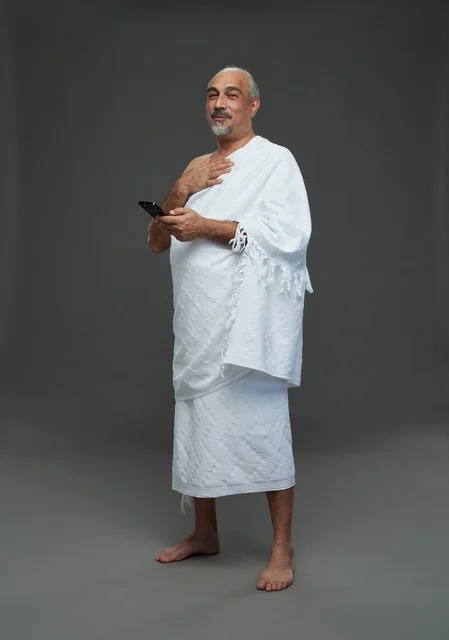 رجل عربي بملابس الإحرام يحمل هاتف ذكي في الاستوديو