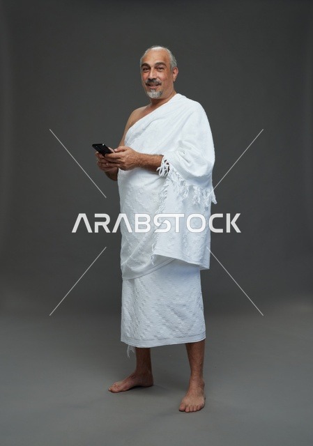 رجل عربي بملابس الإحرام يحمل هاتف ذكي في الاستوديو