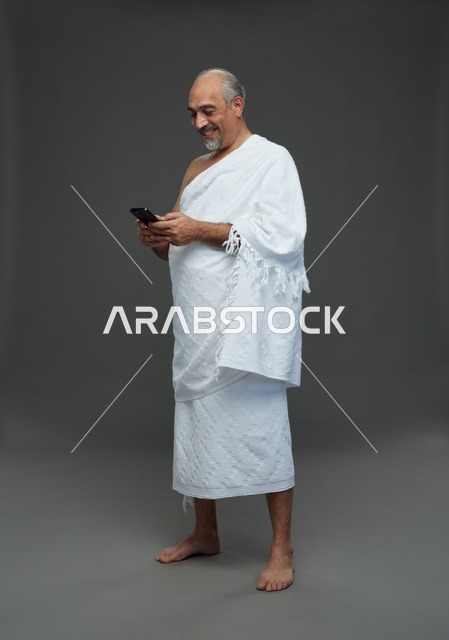 Arab Pilgrim in Ihram Using Smartphone on Gray Background