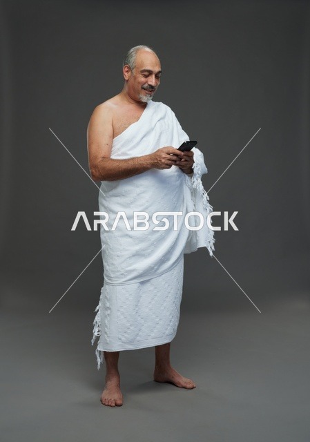 رجل عربي بملابس الإحرام يستخدم الهاتف الذكي في الاستوديو