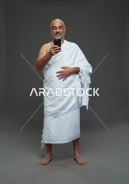 رجل سعودي بملابس الإحرام يستخدم الهاتف الذكي في استوديو