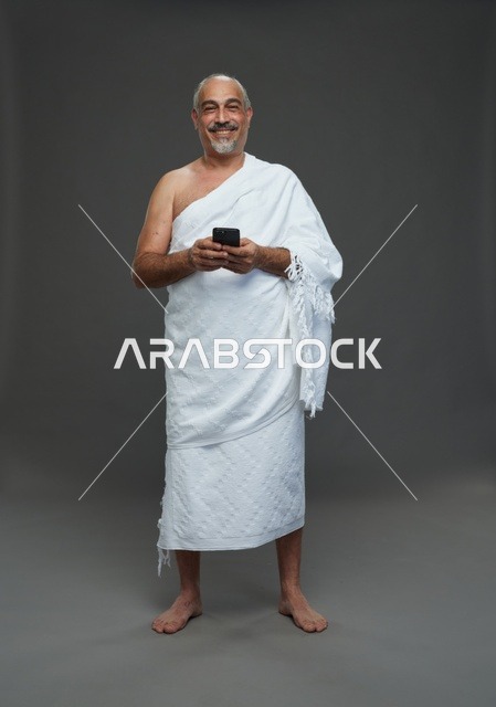 رجل سعودي بملابس الإحرام يحمل هاتفاً ذكياً في الاستوديو