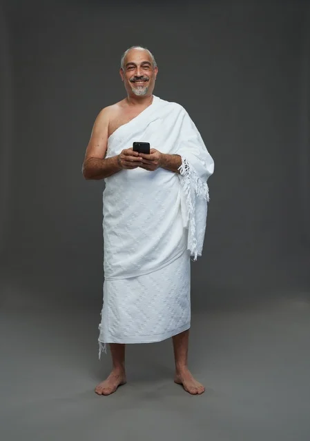 رجل سعودي بملابس الإحرام يحمل هاتفاً ذكياً في الاستوديو