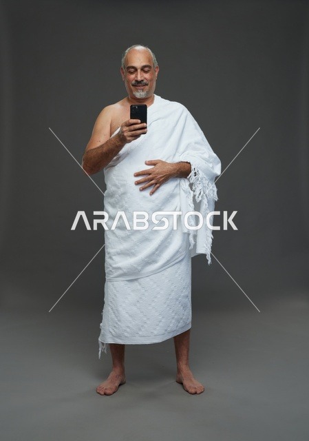 Saudi Man in Ihram Using Smartphone on Grey Background