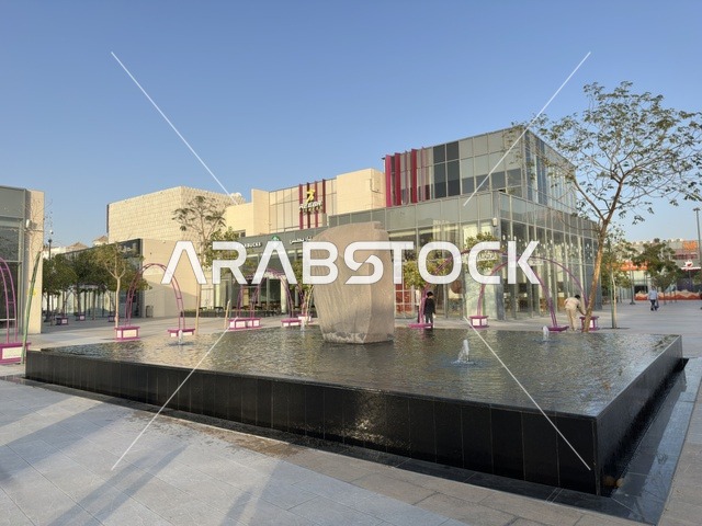 A modern commercial plaza with a water fountain and contemporary buildings in the Shurfat Park complex in Khobar City, Saudi Arabia.