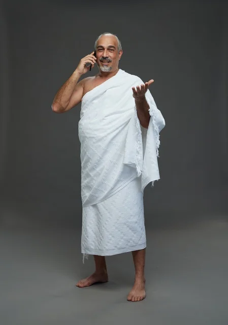 رجل سعودي يرتدي ملابس الإحرام ويتحدث عبر الهاتف الذكي