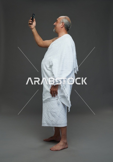 رجل سعودي بملابس الإحرام يلتقط سيلفي بخلفية رمادية