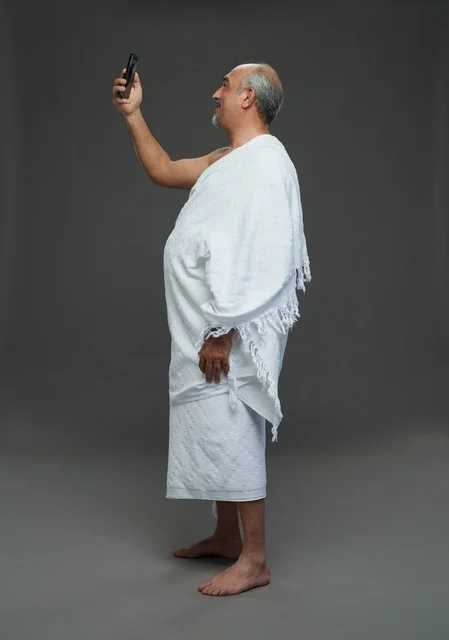 رجل سعودي بملابس الإحرام يلتقط سيلفي بخلفية رمادية
