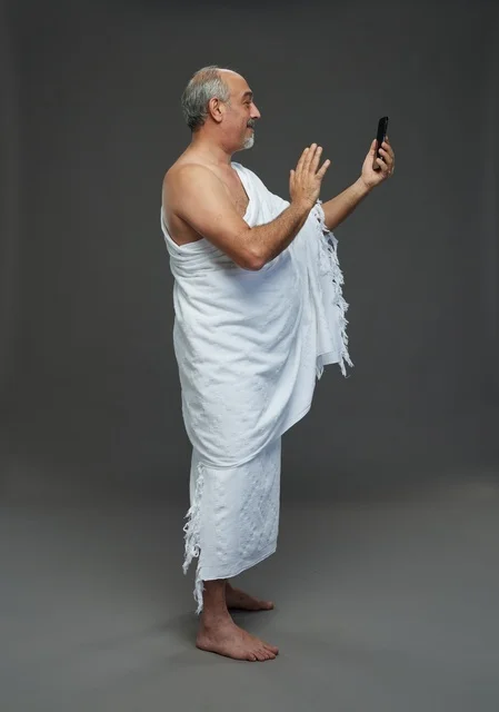 Saudi Man in Ihram Using Smartphone on Grey Background