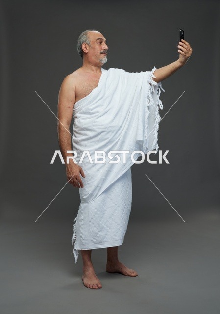 رجل سعودي بملابس الإحرام يلتقط سيلفي باستخدام الهاتف الذكي