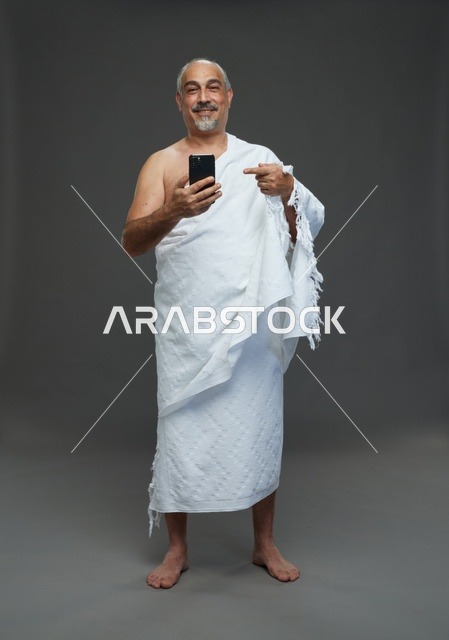 رجل سعودي بملابس الإحرام يشير إلى هاتف ذكي