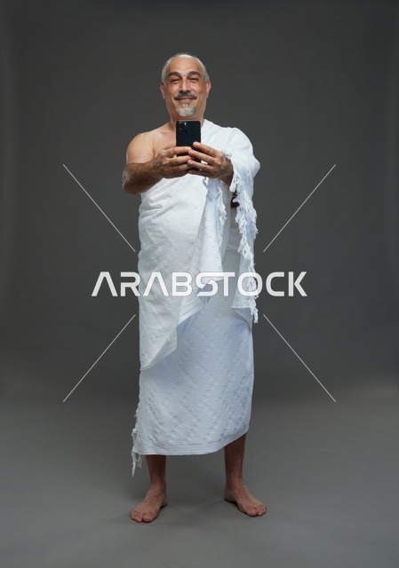 رجل سعودي بملابس الإحرام يلتقط سيلفي بهاتف ذكي في استوديو