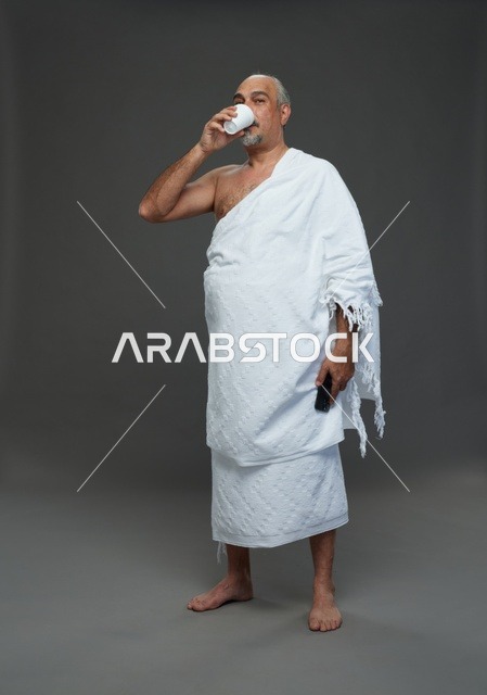 رجل سعودي بملابس الإحرام يشرب الماء ويحمل هاتف