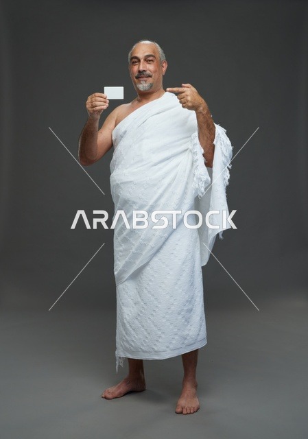 رجل سعودي بملابس الإحرام يحمل بطاقة فارغة في الاستوديو
