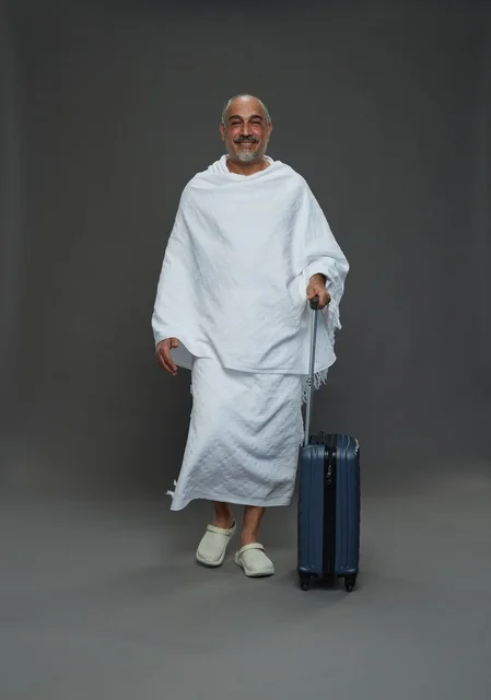 رجل سعودي بملابس الإحرام مع حقيبة سفر في استوديو رمادي
