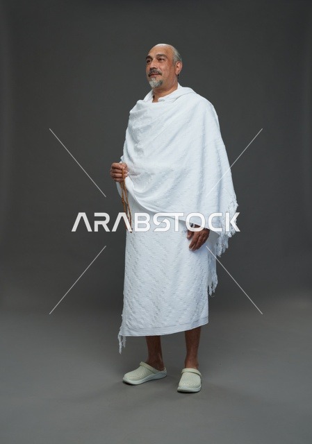 رجل سعودي بملابس الإحرام البيضاء يمسك مسبحة في الاستوديو