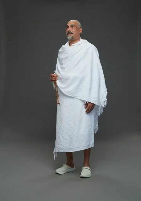 رجل سعودي بملابس الإحرام البيضاء يمسك مسبحة في الاستوديو
