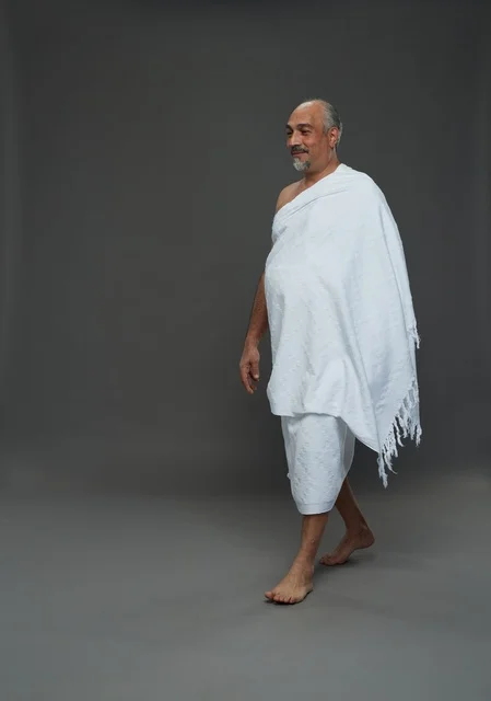 رجل سعودي بملابس الإحرام يمشي خلفية رمادية