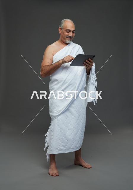 رجل سعودي بملابس الإحرام يستخدم جهازاً لوحياً