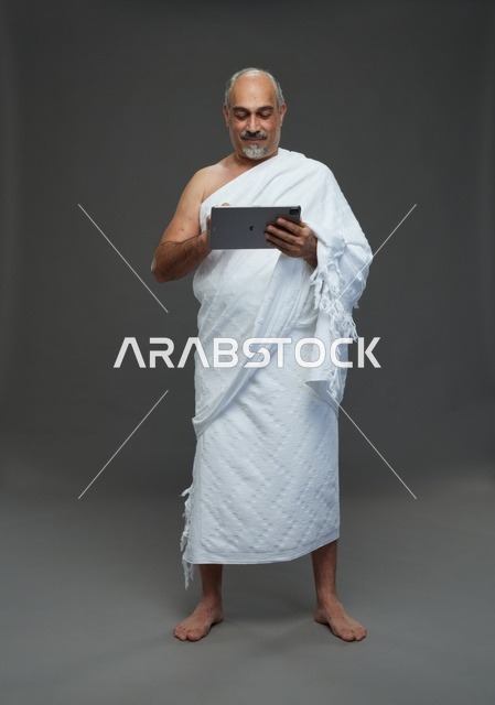 رجل سعودي بملابس الإحرام يستخدم جهازاً لوحياً