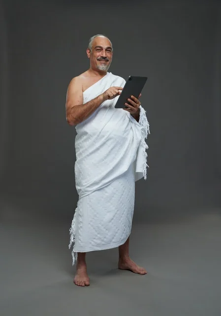 رجل سعودي بملابس الإحرام يستخدم تابلت بخلفية رمادية