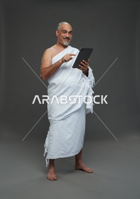 Saudi Man in Ihram Using Tablet on Grey Background