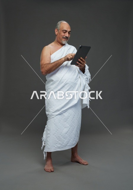 رجل سعودي بملابس الإحرام يستخدم جهازا لوحيا