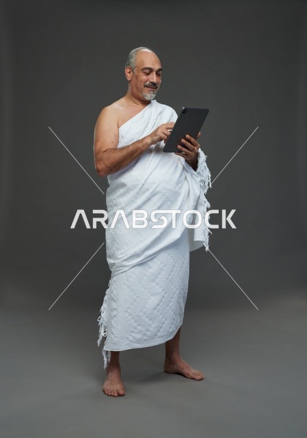 رجل سعودي بملابس الإحرام يستخدم جهاز لوحي في الاستوديو
