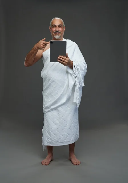 رجل سعودي بملابس الإحرام يستخدم تابلت بخلفية رمادية