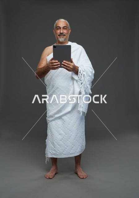 رجل سعودي بملابس الإحرام يستخدم جهازًا لوحيًا