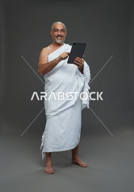 رجل سعودي بملابس الإحرام يستخدم جهازاً لوحياً في الاستوديو