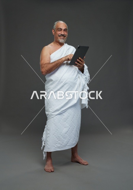 رجل سعودي بملابس الإحرام يستخدم جهازاً لوحياً