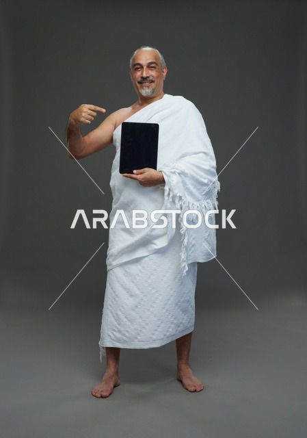 رجل سعودي بملابس الإحرام يحمل جهازاً لوحياً