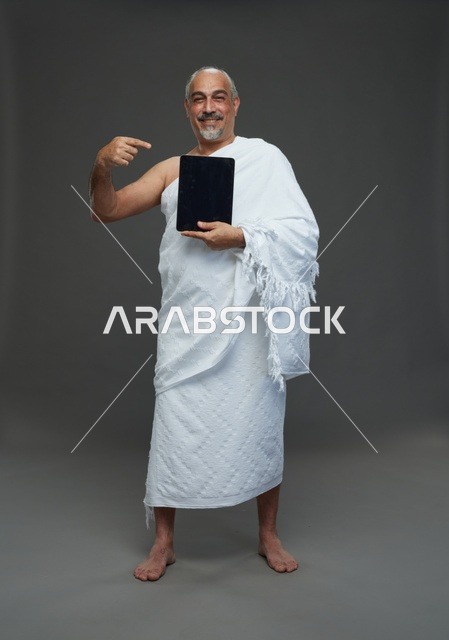 رجل سعودي بملابس الإحرام يشير إلى جهاز لوحي