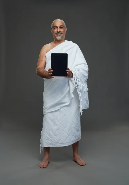 Saudi Man in Ihram Holding Tablet on Grey Background