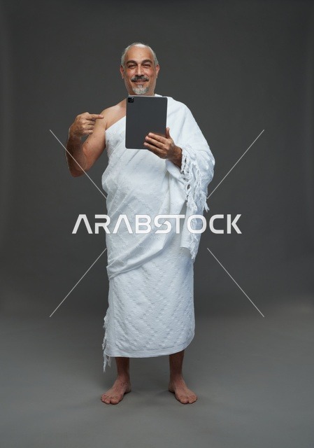 Saudi Man in Ihram Using Tablet on Gray Background