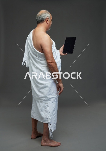 رجل سعودي بملابس الإحرام يستخدم جهازاً لوحياً