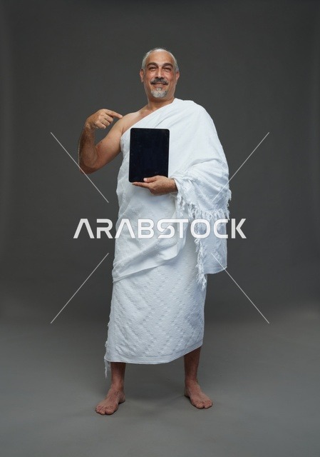 رجل سعودي بملابس الإحرام يحمل جهازاً لوحياً
