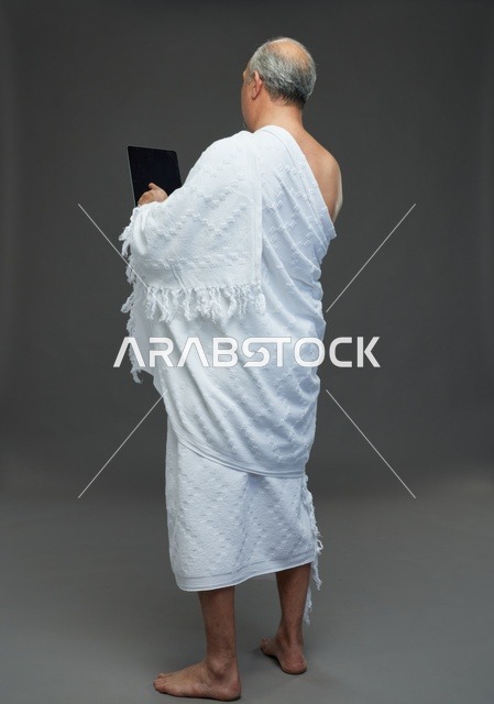 Saudi Man in Ihram Using Tablet on Grey Background