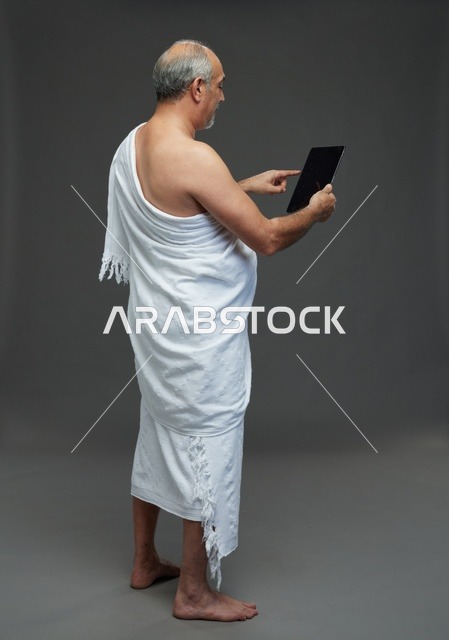 رجل سعودي بملابس الإحرام يستخدم جهاز لوحي في استوديو