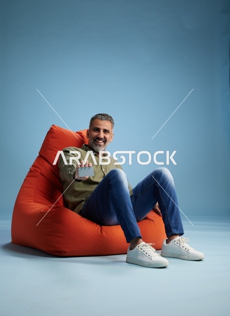 رجل سعودي يحمل بطاقة ائتمان على كرسي أحمر