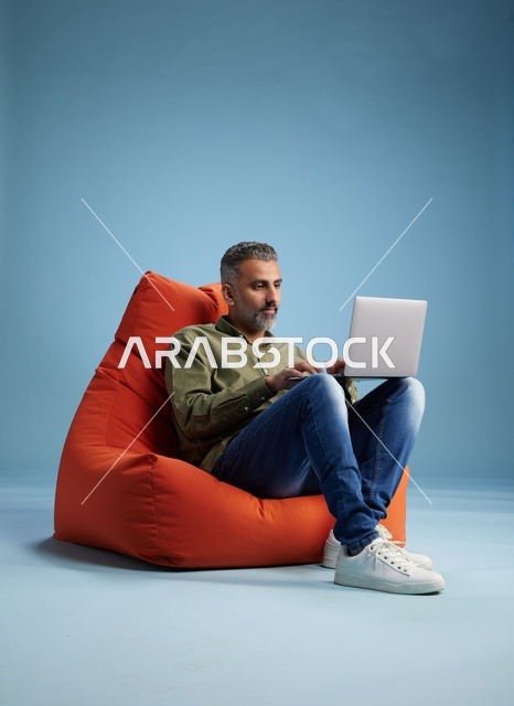 رجل سعودي يعمل على لابتوب فوق بين باج برتقالي