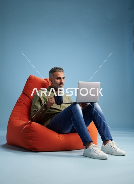 رجل سعودي يعمل على كمبيوتر محمول في كرسي مريح