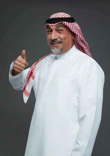 رجل سعودي بالزي التقليدي يبتسم ويشير بالإبهام للأعلى