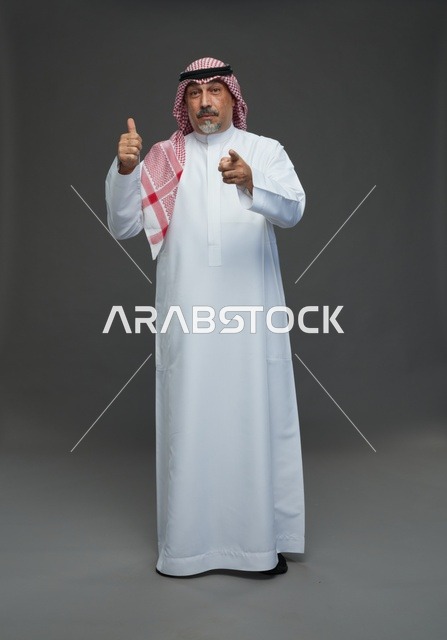 رجل سعودي بالزي التقليدي يرفع إبهامه ويشير للكاميرا
