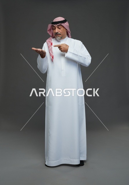 رجل سعودي بالثوب التقليدي يشير لراحة يده في الاستوديو